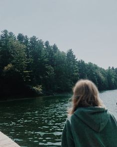 a person standing on a dock looking out at the water and trees in the background