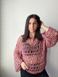 a woman wearing a pink crochet sweater posing with her hands on her head