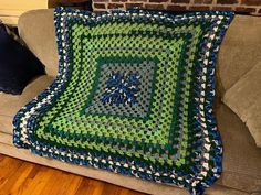 a green and blue afghan sitting on top of a couch next to a brick wall