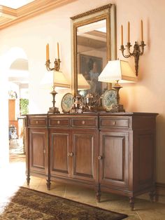 a large mirror is on the wall above a buffet table with two lamps and plates