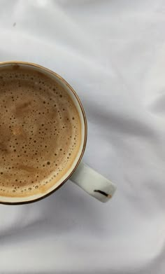 a cup of coffee sitting on top of a white tablecloth covered bed sheet with a spoon in it