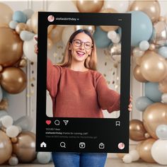 a woman holding up a photo frame with balloons in the background