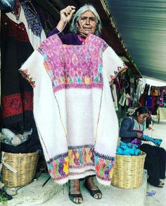 an old woman holding up a colorful sweater in front of some baskets and other items