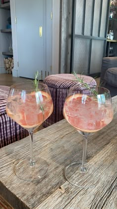 two wine glasses filled with pink liquid sitting on top of a wooden table next to a couch