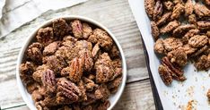 a white bowl filled with pecans next to a baking sheet on top of a wooden table