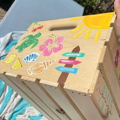 a child's hand holding a wooden box with stickers on it