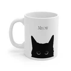 a white coffee mug with a black cat's face and the words meow on it