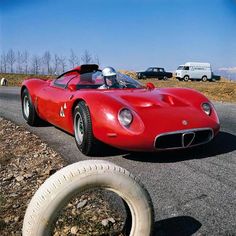 a red sports car is parked on the side of the road next to an old tire