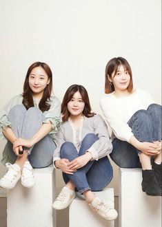 three young women sitting on top of white cubes with their arms crossed and legs crossed