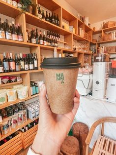 a person holding up a coffee cup in front of shelves