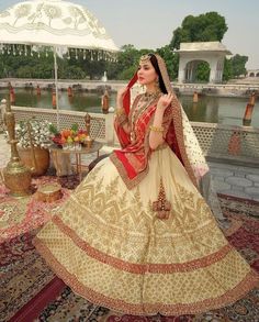 a woman in a white and red wedding dress is sitting on a rug with an umbrella over her head