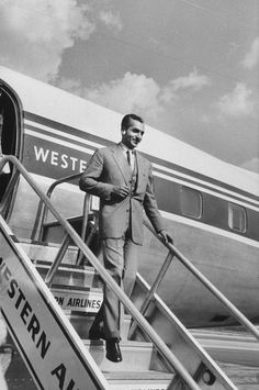 a black and white photo of a man walking down the stairs to an air plane