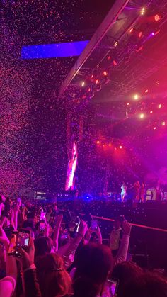 a large crowd is at a concert with confetti falling from the ceiling and people taking pictures on their cell phones