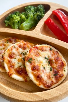 two small pizzas on a wooden plate with broccoli and peppers