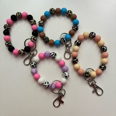 three bracelets with different colored beads and skulls are on a white surface, one has a pair of scissors