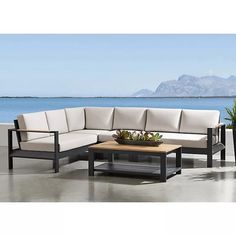 an outdoor sectional sofa with coffee table and potted plant in front of the ocean