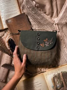 a hand holding an open book next to a purse on top of a table filled with books