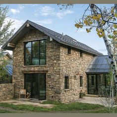 a stone house with glass windows on the front and side walls, surrounded by trees