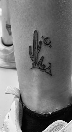 a small cactus tattoo on the side of a woman's leg, with moon and stars above it