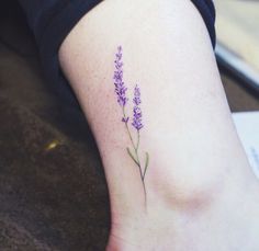 a purple flower tattoo on the left side of the leg, with words below it