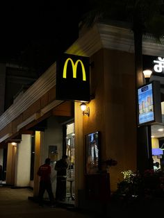 a mcdonald's restaurant at night with people standing outside