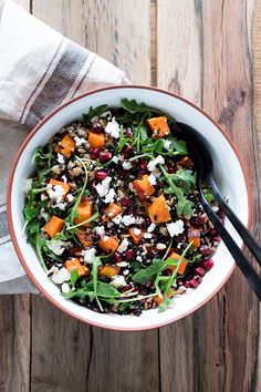 a white bowl filled with salad on top of a wooden table next to a napkin