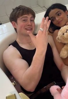 a young man and woman sitting in a bathtub with a teddy bear on their lap