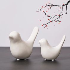 two white birds sitting next to each other on top of a wooden table in front of a branch with red berries