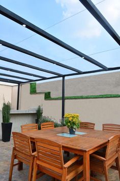 an outdoor dining table and chairs under a pergolated roof with potted plants