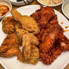 fried chicken and other foods on a white plate with sauces in bowls behind it