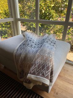 a blanket sitting on top of a white couch next to a large window with trees in the background