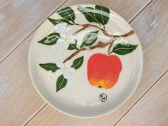 a white plate with an apple painted on the side and leaves, flowers, and branches