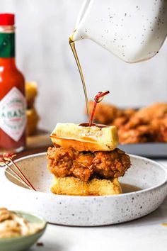 a person pouring sauce onto a sandwich on a plate