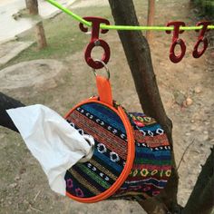 an orange purse hanging from a tree in the park with some clothes hanging on it