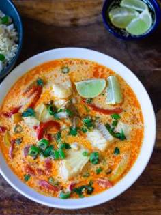 a white bowl filled with soup and garnished with green onions, red peppers, and lime