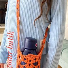 a woman wearing an orange crocheted bag with a bottle in it's pocket