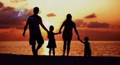 a family holding hands while walking on the beach at sunset with the sun setting in the background