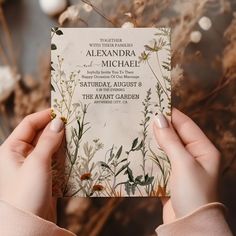 a person holding up a wedding card in front of some dried plants and flowers on the ground