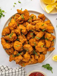 a white plate topped with fried cauliflower next to lemon wedges and ketchup