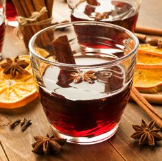 two glasses filled with mulled and cinnamon on top of a wooden table next to orange slices