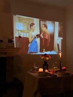 a table with candles and wine glasses on it in front of a large television screen