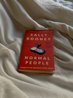 a red book sitting on top of a bed covered in white sheets and linens