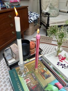 two candles are sitting on top of books and magazines in a living room with a chair