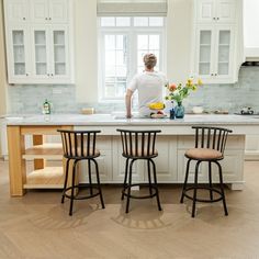 a woman standing at the counter in a kitchen with three stools next to it