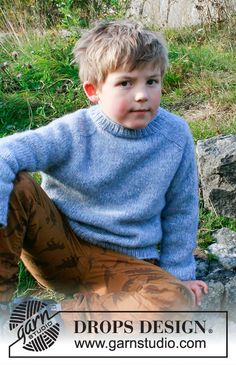 a young boy sitting on the ground wearing a blue sweater