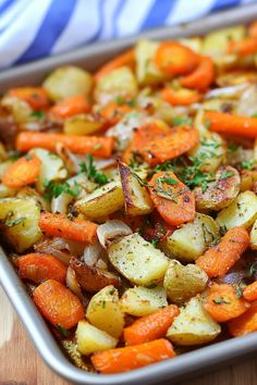 a pan filled with potatoes and carrots on top of a wooden table