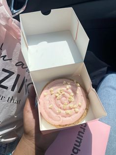 a pink frosted doughnut in a box on someone's lap with the lid open