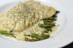 a white plate topped with fish covered in sauce and asparagus