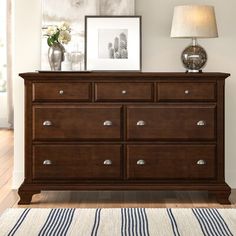 a wooden dresser sitting on top of a hard wood floor next to a lamp and pictures