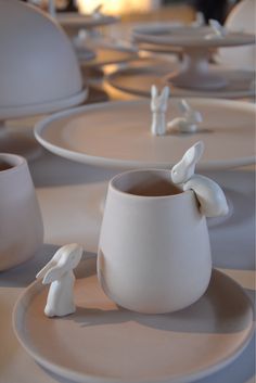 some white plates and cups with small figurines sitting on top of them in the shape of rabbits